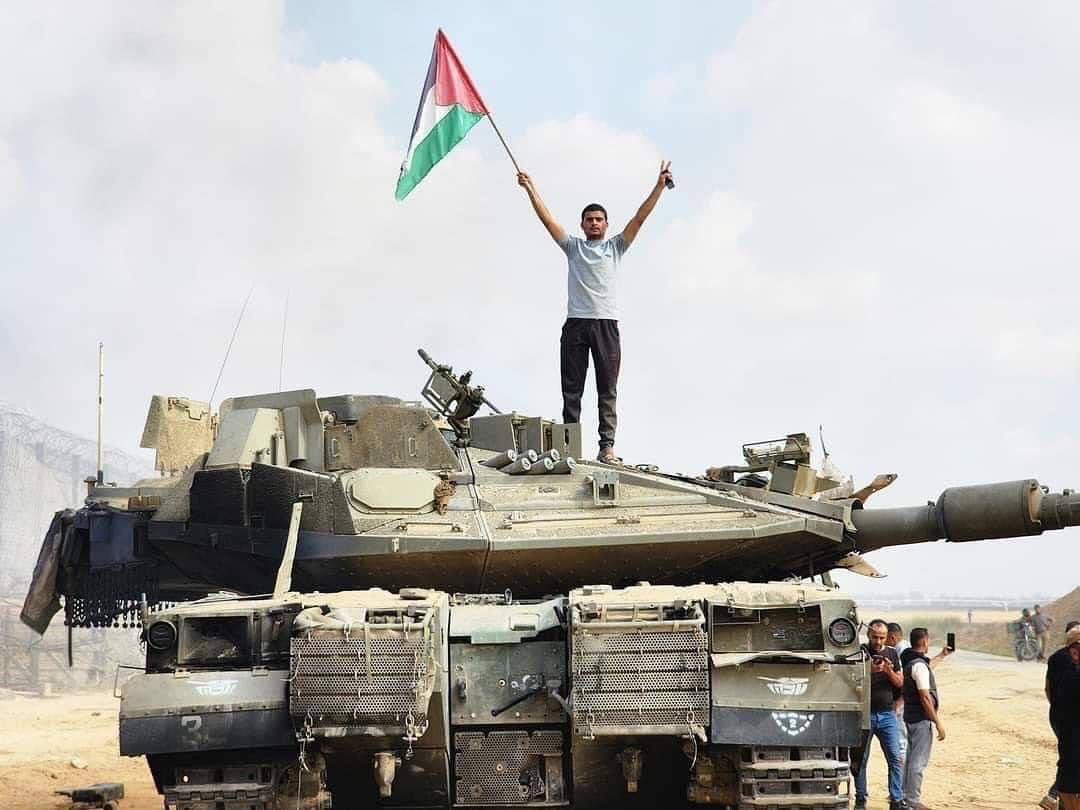 فلسطيني يرفع راية بلاده على ظهر دبابة لقوات الاحتلال جرى إحراقها